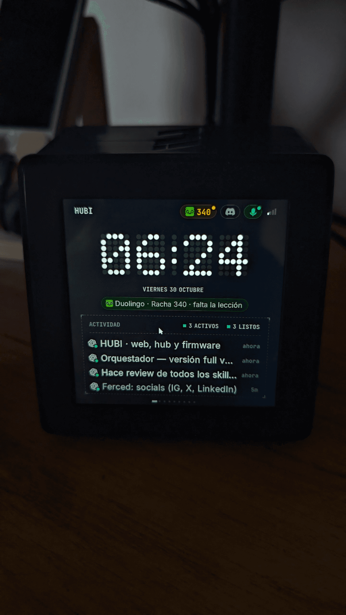 HUBI físico mostrando el reloj, un recordatorio de Duolingo y actividad de agentes de programación